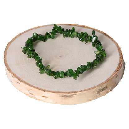 Green diopside bracelet chips on wooden display, showcasing vibrant gemstone jewelry.