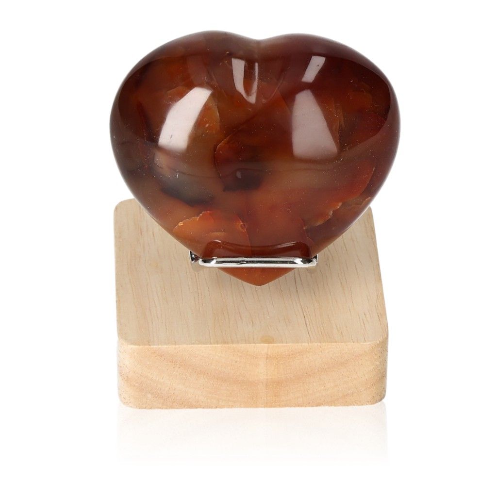 Carnelian heart gemstone on a wooden stand, symbolizing energy and motivation for facing challenges and achieving goals.